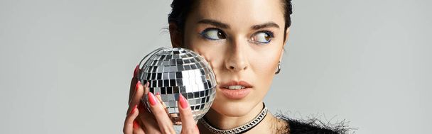 A young woman with short dyed hair poses in stylish attire, holding a disco ball in front of her face. - Photo, image