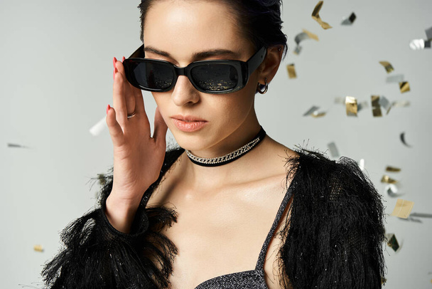 A fashionable young woman with short dyed hair striking a pose in a chic black dress and trendy sunglasses. - Fotografie, Obrázek