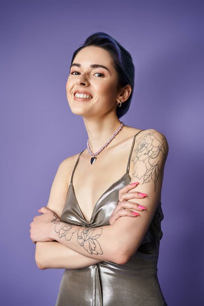 A young woman with blue hair strikes a pose in a stunning silver dress, showcasing intricate tattoos on her arms. - Photo, image