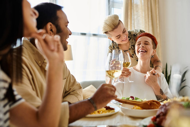 Un grupo diverso de amigos compartiendo una comida alrededor de una mesa, incluyendo una pareja lesbiana cariñosa. - Foto, imagen