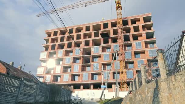 Modern Urban Construction Site Under Development, A large multistory building under construction in an urban setting, featuring a towering crane and unfinished brick facade basking in sunlight - Footage, Video