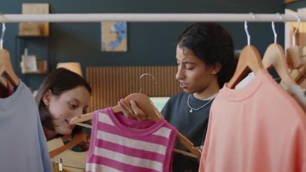 Medium shot of Biracial teenage girl taking clothes on hangers from rack while helping her Caucasian female friend with cerebral palsy to choose daily outfit at home - Footage, Video
