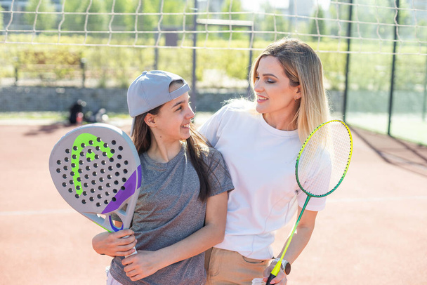 Happy caucasian mother and daughter playing padel tennis and badminton on tennis court outdoors. High quality photo - Photo, Image