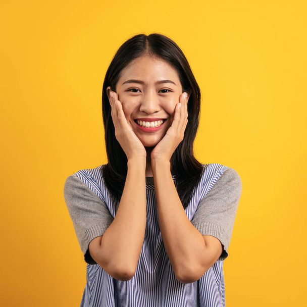 Fiatal ázsiai nő alkalmi ruhák borító arc kezével és mosolyogva örül, miközben áll elszigetelve sárga háttér. - Fotó, kép