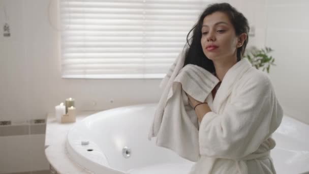 Μέτριο πλάνο της ελκυστικής γυναίκας σε λευκό μπουρνούζι σκούπισμα μακριά μαλλιά με πετσέτα στο μπάνιο στο σπίτι - Πλάνα, βίντεο