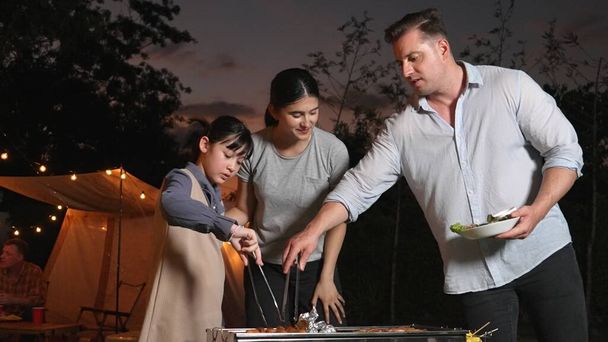 Family celebrate holiday in garden. Father, mother and child grill food for member. Outdoor camping activity to relax with meal and spend time with young generation cross generation gap. Divergence. - Photo, Image