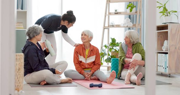 Senior woman, exercise group and personal trainer on floor, home and talk for training advice, workout or health. Elderly lady, team and fitness coaching with chat, drinking water and relax in house. - Photo, Image