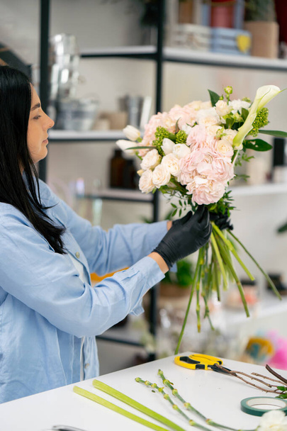 bloemenwinkel een meisje in de buurt van een witte tafel verzamelt een bloemstuk van een mooi boeket van witte bloemen - Foto, afbeelding