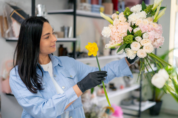 квітковий магазин дівчина біля білого столу збирає квіткову композицію красивого букета з білих квітів - Фото, зображення