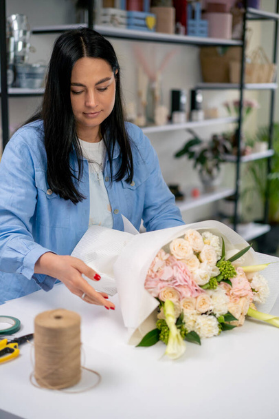 in een bloemenwinkel wikkelt een bloemist een kant-en-klaar delicaat boeket in een witte papieren wikkel - Foto, afbeelding