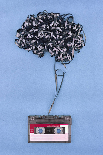 Concept with mental health protection by music. Vintage cassette tape with exposed tape in the form of brain. Chambray blue color paper background. - Photo, Image