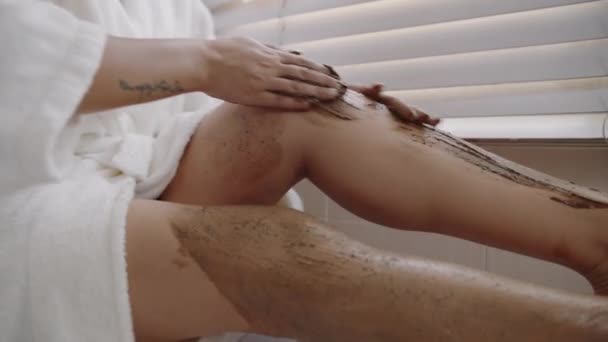Cortado tiro de mujer irreconocible haciendo masaje de piernas con exfoliante de chocolate al tomar baño - Metraje, vídeo