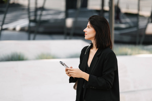 Young successful confident woman is holding her phone outdoors on a sunny day in the sity. - Foto, imagen