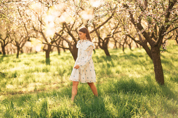 Jonge vrouw draagt witte jurk lopen gratis in amandel boomgaard op een zonnige dag. - Foto, afbeelding