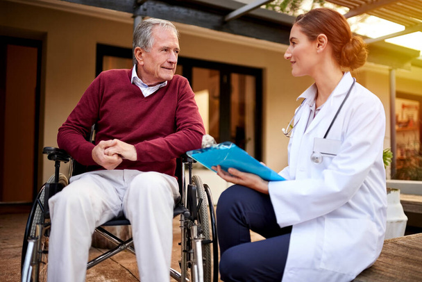 Senior, doctor and notes on person in wheelchair with consultation, advice and healthcare checklist. Medical, insurance and elderly man with disability trust in support or help of caregiver at home. - Photo, Image
