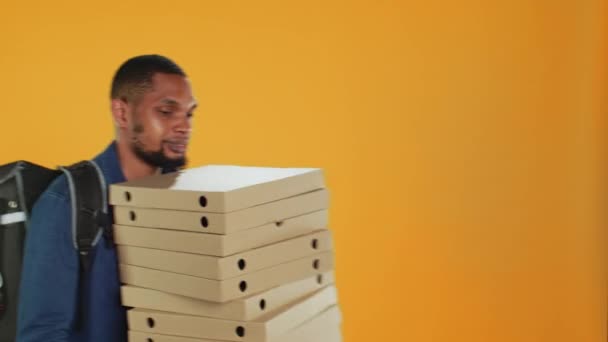 Corriere pizzeria maschile che trasporta un enorme mucchio di scatole di pizza in studio, preparandosi a consegnare l'ordine dei pasti ai clienti. Un giovane fattorino con una grossa pila di fast food da asporto, spedizione. Camera A. - Filmati, video