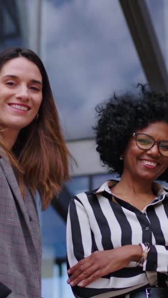 垂直ローアングル。 ビルオフィスの前で立っているフォーマルなスーツの多様なビジネス女性の笑顔のグループは陽気に見えます. エンパワーされた女性起業家アームが交差 - 映像、動画