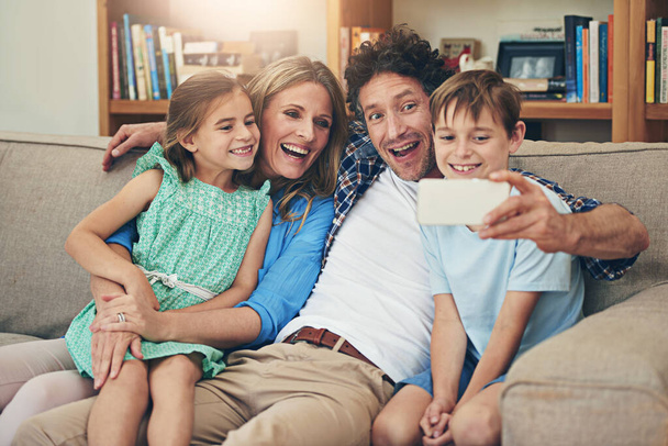 Οικογένεια, selfie και γονείς με παιδιά, καναπές και γέλιο για αστείο από τον μπαμπά, αστείο πρόσωπο και κωμωδία στο σπίτι. Σπίτι, γυναίκα και άνδρας με παιδιά, μαζί και σύνδεση με τη φωτογραφία για τη μνήμη στο τηλέφωνο. - Φωτογραφία, εικόνα