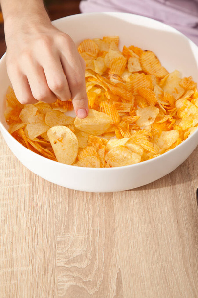 Caucasian person in pink t-shirt holding white plate full of potato chips and preparing to eat - Photo, Image