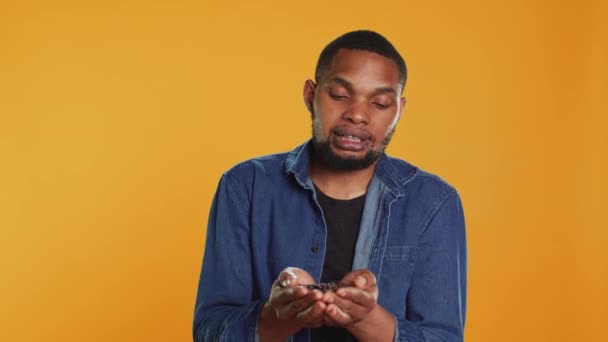 African american cheerful guy posing with black roasted coffee beans against orange background, caffeine lover. Young person recommending arabics flavored americano coffee seeds. Camera A. - Footage, Video
