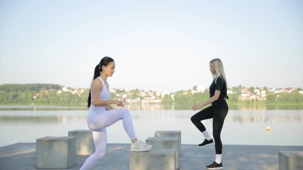 Fitness training van twee vrouwen buiten op de achtergrond van het meer. Actieve fitness oefeningen op een warme zomerdag. Het begrip gezondheid, verkeer. - Video