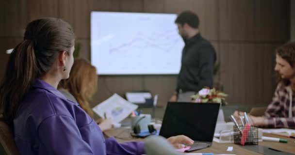 Üzletemberekből álló csoport egy vállalati tárgyalóban, növekedési táblázatokat vitatva meg, háttérben egy prezentációval. Eljegyzett csapattagok modern irodai környezetben. - Felvétel, videó