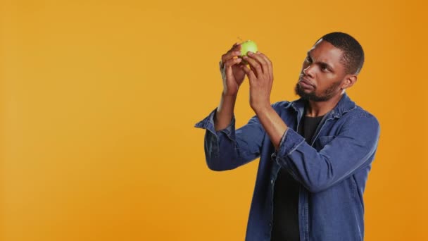 Αρσενικό μοντέλο που εξετάζει ένα πράσινο μήλο για να είναι καθαρό μετά τη συγκομιδή, εξασφαλίζοντας την ωριμότητα των τοπικών φρούτων. Νέοι ενήλικες υποστηρίζουν την έννοια του βιώσιμου τρόπου ζωής. Κάμερα Β. - Πλάνα, βίντεο