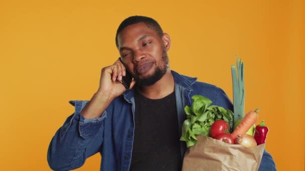 Afro-Amerikalı bir adam market alışverişinde telefonda sohbet ediyor, insanlarla şehirdeki yeni bir sıfır atık eko mağazası hakkında konuşuyor. Genç yetişkin taze biyo-ürün tavsiye ediyor. Kamera A. - Video, Çekim