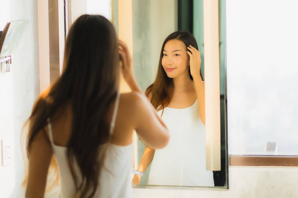 Portrait belle jeune femme asiatique vérifier son visage et le visage dans la salle de bain intérieure - Photo, image