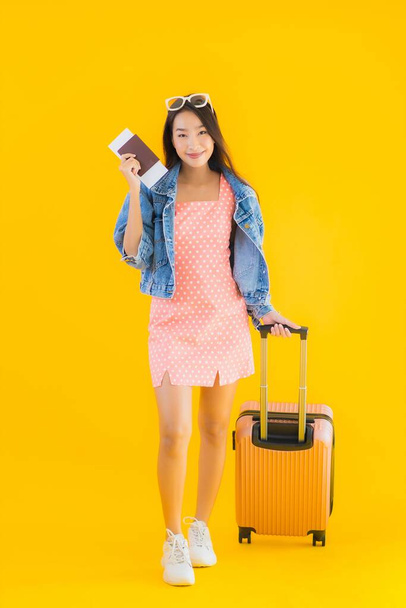 Porträt schöne junge Asiatin mit Reisetasche mit Reisepass und Bordkarte auf gelbem Hintergrund - Foto, Bild