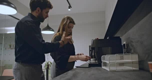 Deux collègues prennent une pause café dans une cuisine de bureau moderne. L'un préparant le café, l'autre vérifiant le téléphone. Environnement de travail occasionnel. - Séquence, vidéo