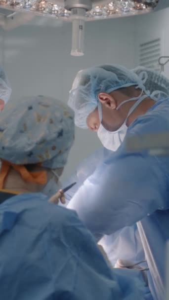 Érett férfi sebész sebészeti ruhában, kollégákkal a műtőben. A fiatal nővér asszisztál az orvosoknak és orvosi műszereket ad. Szakmai orvosok öltés seb és befejező műtét. - Felvétel, videó