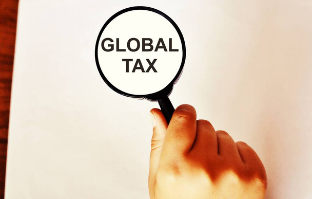 Szkło powiększające stos pieniędzy z napisem "Globalny podatek". Koncepcja nowego podatku europejskiego. - Zdjęcie, obraz