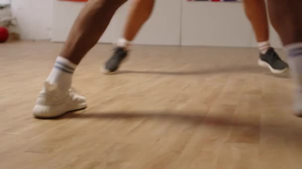 2つの認識できないバスケットボールプレーヤーの低いセクションの遅い動きは,屋内でパーケットフロアでプレーしながらゴールを獲得しようとボールをドリブルして跳ねます - 映像、動画