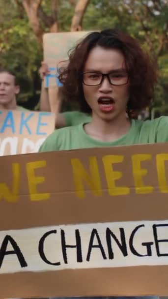 Вертикальный портрет азиатского эко-активиста, держащего плакат при участии в акции протеста в парке с друзьями - Кадры, видео