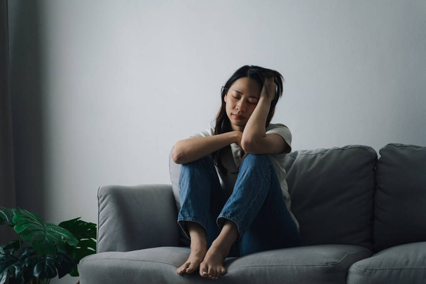 Unhappy lonely depressed woman is sitting on the couch and holding her head. She looks sad and tired. - Photo, Image