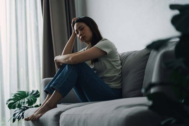 Несчастная одинокая депрессивная женщина сидит на диване и держит голову. Она выглядит грустной и уставшей.. - Фото, изображение
