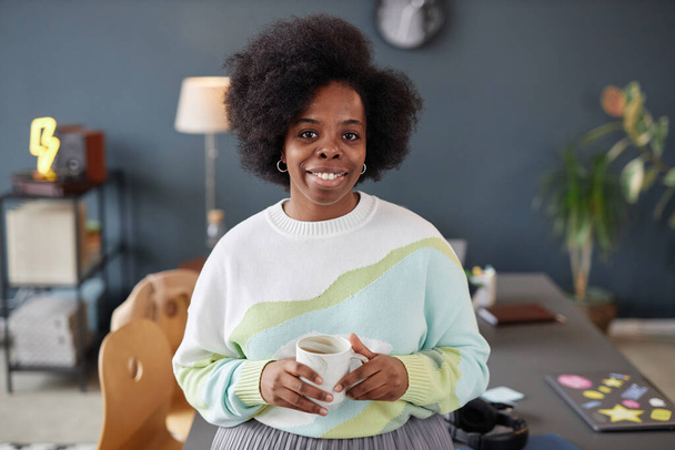 Minimális derék fel portré mosolygós afro-amerikai nő természetes göndör haj nézi kamera álló irodai beállítás és gazdaság bögre másolási hely - Fotó, kép