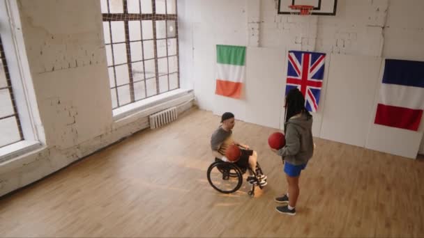 Vue d'en haut du jeune homme caucasien handicapé assis en fauteuil roulant et pratiquant des lancers francs avec ballon de basket, s'entraînant à l'intérieur avec Biracial entraîneur féminin l'aidant - Séquence, vidéo