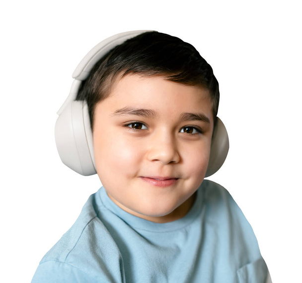 Hymyilevä poika kuulokkeissa, isoalattu iloinen lapsi langattomissa kuulokkeissa kuuntelemassa musiikkia ja katsomassa kameraa valkoisella taustalla leikkauspolulla, Home Educational technology and music concept - Valokuva, kuva