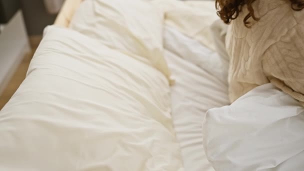 Μια νεαρή γυναίκα χαλαρώνει στο κρεβάτι, απολαμβάνοντας την ηρεμία σε ένα άνετο υπνοδωμάτιο, απεικονίζοντας την άνεση και τον οικιακό τρόπο ζωής. - Πλάνα, βίντεο