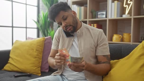 Чоловік рахує канадські долари на дивані в приміщенні під час розмови на мобільному телефоні - Кадри, відео