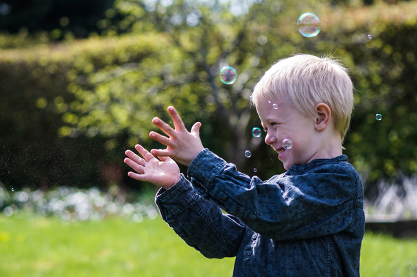 Один маленький хлопчик дме мильні бульбашки в саду в літній день
 - Фото, зображення