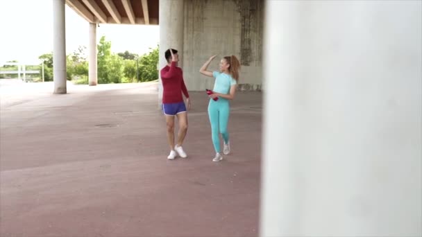 Fiatal pár sportos viselet pacsizás közben egy szabadtéri edzés alatt egy híd alatt. - Felvétel, videó