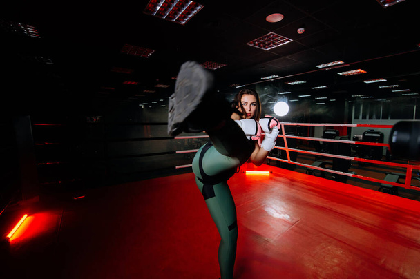 Volledige shot van stijlvolle jonge vrouw atleet in zwarte sportkleding staan in boksring, tillen een been, doen high kick, vechten tegen onzichtbare vijand. Sport, vechtsport en kickboksen - Foto, afbeelding