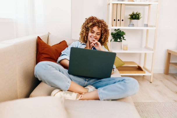Örömteli nő dolgozik laptop, körülvéve kényelmes otthoni kényelmet. - Fotó, kép