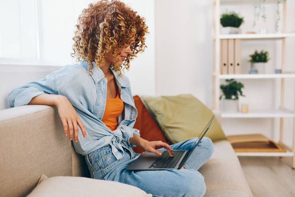 Femme souriante tapant sur ordinateur portable, travaillant de la maison dans un salon confortable - Photo, image