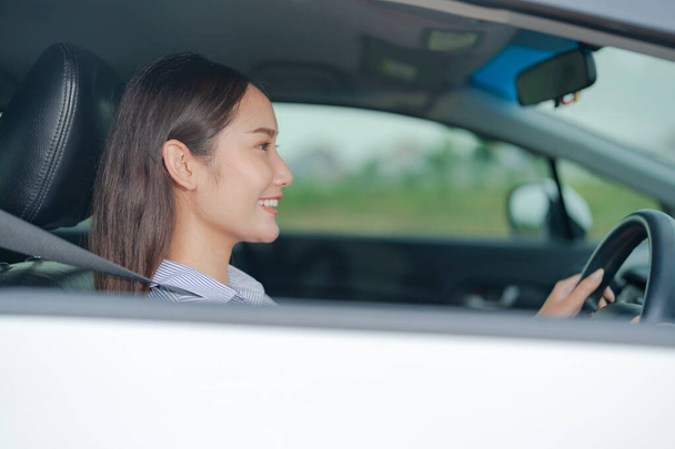 Giovane donna sorridente seduta sul sedile del conducente, che tiene con fiducia il volante di un'auto con un'espressione luminosa e allegra, evidenziando una guida sicura e piacevole - Foto, immagini