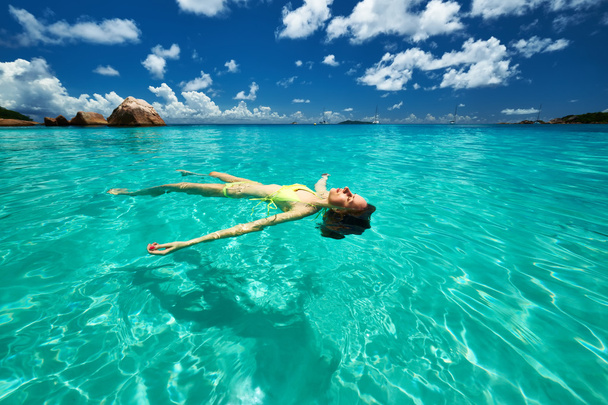 水の上に横たわる黄色ビキニの女性 - 写真・画像