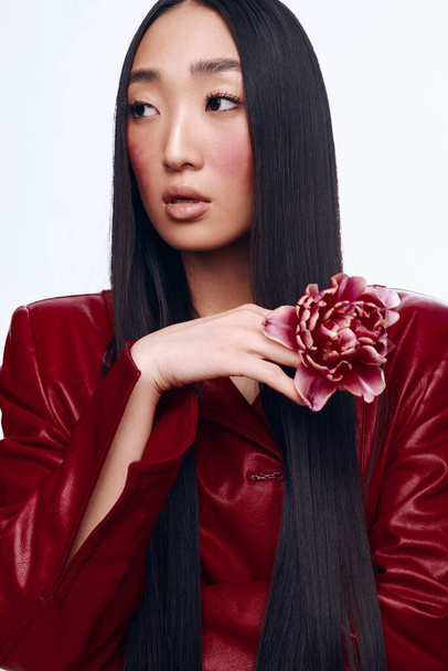 Hermosa mujer asiática con el pelo largo y negro en una chaqueta roja con una delicada flor en la mano - Foto, imagen